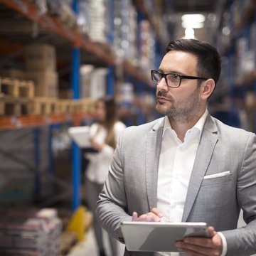 portrait-of-successful-businessman-manager-ceo-holding-tablet-and-walking-through-warehouse-storage-area-looking-towards-shelves.jpg